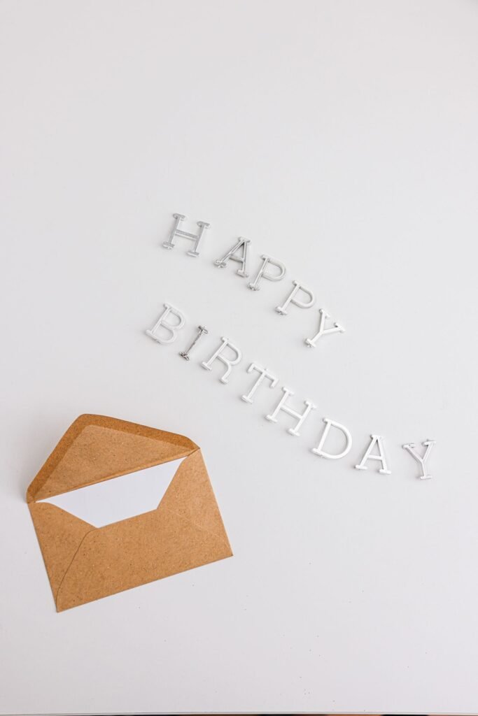 Otvorena papirna koverta sa čestitkom pored slova Happy Birthday na svetloj podlozi.